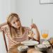 Teen girl in striped shirt at breakfast table with fruits, bread, and juice. Casual morning setting.